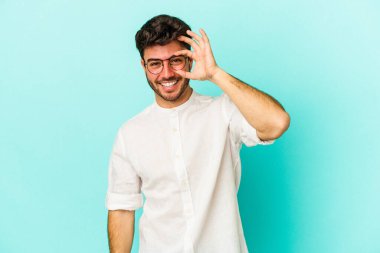 Kafkasyalı genç adam mavi arka planda izole edildi. Heyecanlı görünüyor..