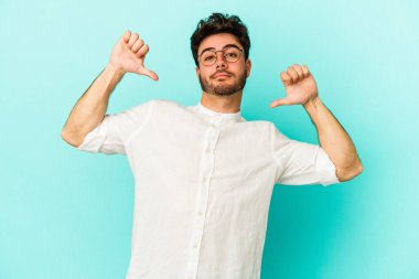 Mavi arka planda izole edilmiş genç beyaz adam gururlu ve kendinden emin hissediyor, örnek olarak.