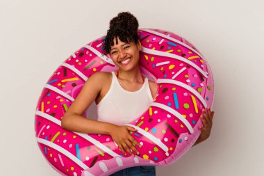 Beyaz arka planda izole edilmiş şişme bir donut tutan genç melez kadın mutlu, güler yüzlü ve neşeli..