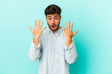 Mavi arka planda izole edilmiş genç beyaz adam on numarayı elleriyle gösteriyor..