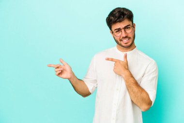 Mavi arka planda izole edilmiş genç beyaz adam işaret parmağıyla fotokopi alanını işaret ederek şok oldu..