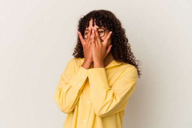 Beyaz arka planda izole edilmiş genç bir ırk kadını parmaklarıyla kameraya göz kırpıyor ve yüzünü kapatmaktan utanıyor..