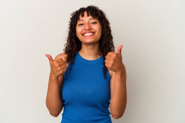 Genç melez bir kadın beyaz arka planda izole edilmiş. Baş parmağını kaldırıyor, gülümsüyor ve kendinden emin..