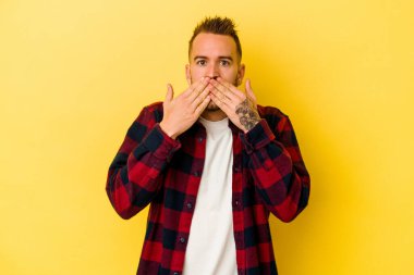 Sarı arka planda izole edilmiş genç dövmeli beyaz adam elleri ile ağzını kapatırken şok oldu..
