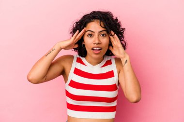 Genç kıvırcık Latin kadın pembe arka planda izole edilmiş hoş bir sürpriz yaşıyor, heyecanlı ve el kaldırıyor..