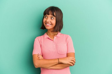 Mavi üzerine izole edilmiş genç bir ırk kadını. Kollarını kavuşturarak gülümsüyor..