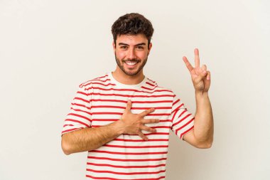 Beyaz arka planda izole edilmiş genç beyaz adam yemin ediyor, elini göğsüne koyuyor..