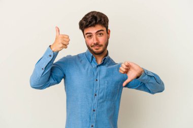 Beyaz arka planda izole edilmiş genç beyaz bir adam baş parmaklarını aşağı ve yukarı kaldırıyor, zor seçim konsepti