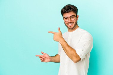 Mavi arka planda izole edilmiş genç beyaz adam işaret parmağıyla fotokopi alanını işaret ederek heyecan ve arzusunu ifade ediyor..