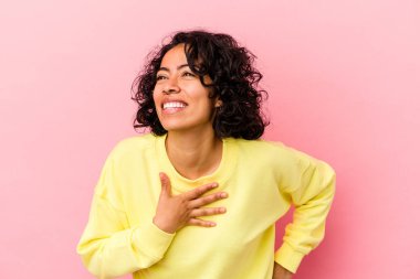 Pembe arka planda soyutlanmış genç kıvırcık Latin kadın gülüyor, ellerini kalbe koyuyor, mutluluk kavramını koruyor..