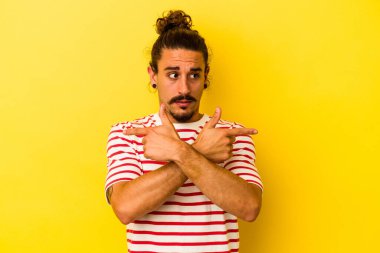 Sarı arka plan noktalarında izole edilmiş uzun saçlı beyaz genç adam iki seçenek arasında seçim yapmaya çalışıyor..