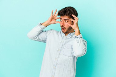 Mavi arka planda izole edilmiş genç beyaz adam bir başarı fırsatı bulmak için gözlerini açık tutuyor..