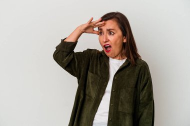 Beyaz arka planda soyutlanmış orta yaşlı beyaz bir kadın çok uzaklara bakıyor ve elini alnına koyuyor..