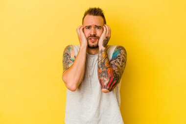 Genç dövmeli beyaz adam sarı arka planda izole edilmiş, ağlıyor, bir şeyden memnun değil, acı ve kafa karışıklığı konsepti..
