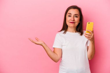 Pembe arka planda cep telefonu tutan orta yaşlı beyaz kadın bir avuç içinde fotokopi alanı ve belinde bir el daha olduğunu gösteriyor..