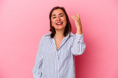 Orta yaşlı beyaz bir kadın pembe arka planda izole edilmiş bir şekilde bir şeylere gülüyor, ağızlarını ellerle kapatıyor..