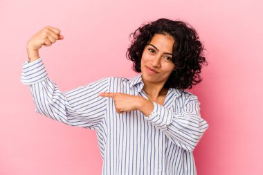 Pembe arka planda soyutlanmış genç kıvırcık Latin kadın kollarıyla güç gösterisi yapıyor, kadınsı gücün sembolü.