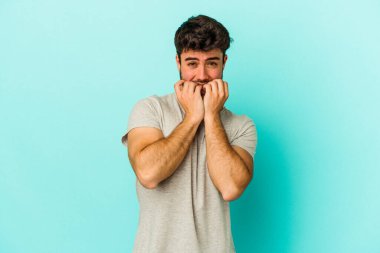 Mavi arka planda izole edilmiş, tırnak yiyen, gergin ve endişeli genç bir beyaz adam..