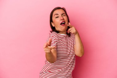 Pembe arka planda izole edilmiş orta yaşlı beyaz kadın parmaklarıyla ön tarafı işaret ediyor..