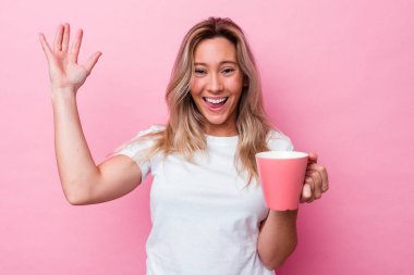 Pembe arka planda pembe kupa tutan genç Avustralyalı kadın hoş bir sürpriz alıyor, heyecanlı ve el kaldırıyor..