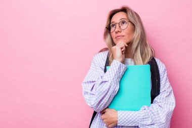 Avustralyalı genç bir öğrenci pembe arka planda izole edilmiş şüpheli ve şüpheci bir ifadeyle yana bakıyor..