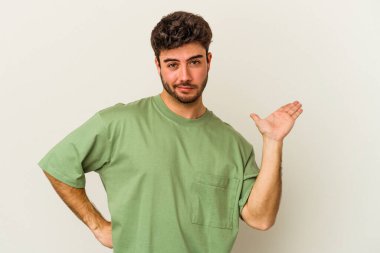 Beyaz arka planda izole edilmiş genç beyaz bir adam sorgulama sırasında omuz silkiyor ve şüphe duyuyor..