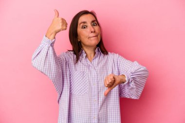 Pembe arka planda soyutlanmış orta yaşlı beyaz bir kadın baş parmağını kaldırıyor ve baş parmağını aşağı gösteriyor, zor seçim konsepti.