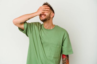 Beyaz arka planda izole edilmiş genç, dövmeli beyaz bir adam. Gözleri ellerle kaplıyor. Gülümsüyor ve bir sürpriz bekliyor..