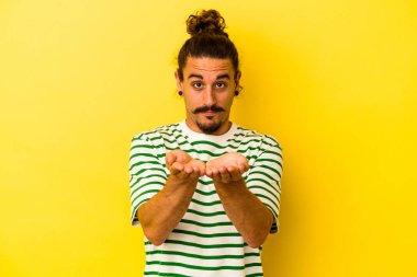 Sarı arka planda izole edilmiş uzun saçlı beyaz bir adam elinde avuç içi bir şeyle kameraya sunuyor..