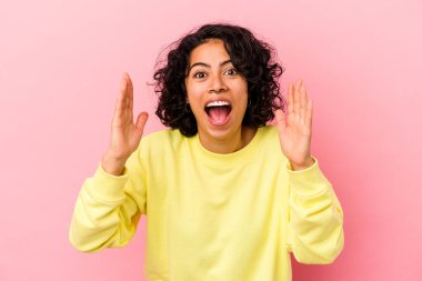 Genç kıvırcık Latin kadın pembe arka planda izole edilmiş hoş bir sürpriz yaşıyor, heyecanlı ve el kaldırıyor..