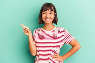 Mavi üzerine izole edilmiş genç melez kadın işaret parmağıyla işaret ederek gülümsüyor..
