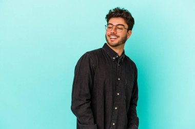 Mavi arka planda soyutlanmış genç beyaz bir adam gülümsüyor, neşeli ve keyifli görünüyor..