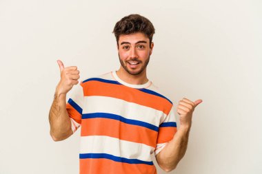 Beyaz arka planda izole edilmiş genç beyaz bir adam iki parmağını da kaldırıyor, gülümsüyor ve kendinden emin..