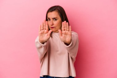 Orta yaşlı, beyaz bir kadın pembe arka planda izole edilmiş elini uzatmış, dur işareti gösteriyor..
