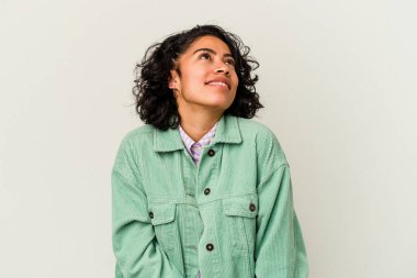 Beyaz arka planda izole edilmiş genç kıvırcık Latin kadın hedeflere ve amaçlara ulaşma hayali kuruyor.