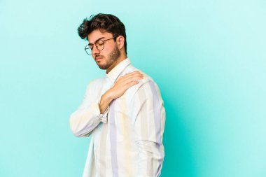 Mavi arka planda izole edilmiş, omuz ağrısı olan genç beyaz bir adam..