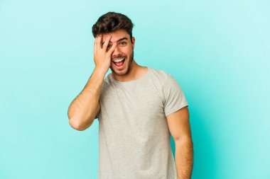 Mavi arka planda izole edilmiş genç beyaz adam yüzünün yarısını palmiye ile kaplayarak eğleniyor..