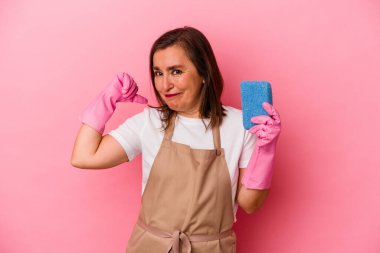 Orta yaşlı beyaz kadın evini temizliyor pembe arka planda soyutlanmış, gururlu ve kendinden emin, örnek olarak..