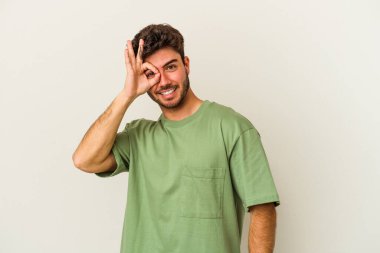 Beyaz arka planda izole genç beyaz adam heyecanlı tamam göz jesti tutmak.