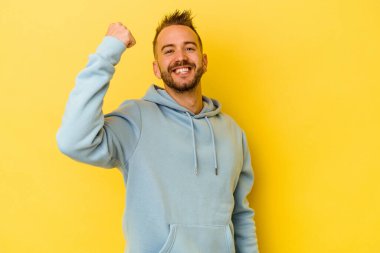 Sarı arka planda izole edilmiş genç dövmeli beyaz adam tasasız ve heyecanlı tezahüratlar yapıyor. Zafer konsepti.