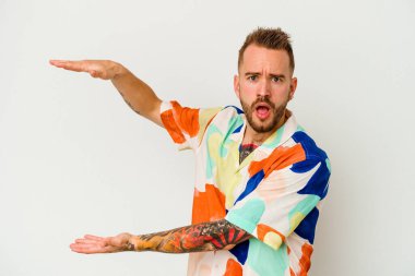 Beyaz arka planda izole edilmiş genç dövmeli beyaz adam elleri arasında bir kopya alanı tutarken şok ve hayrete düştü..