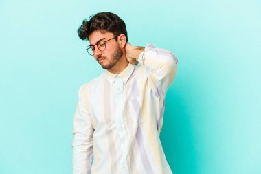 Kafkasyalı genç adam mavi arka planda izole edilmiş. Stres yüzünden boynu ağrıyor. Masaj yapıyor ve elle dokunuyor..