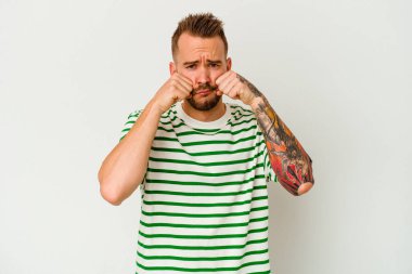 Beyaz arka planda, ağlayan ve sızlanan genç dövmeli beyaz bir adam var..