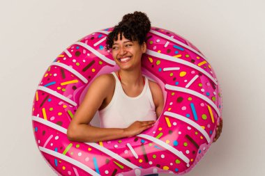 Beyaz arka planda izole edilmiş şişme donut tutan genç bir ırk kadını gülüyor ve eğleniyor..