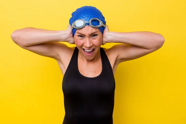 澳大利亚年轻的游泳女子 双手捂住耳朵 用黄色背景隔离 尽量不要听到太大声的声音 — 图库照片