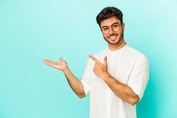 Joven Hombre Caucásico Aislado Sobre Fondo Azul Excitado Sosteniendo Espacio —  Fotos de Stock