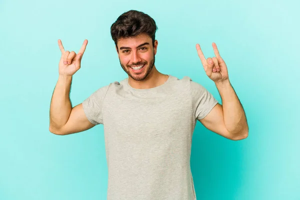 stock image Young caucasian man isolated on blue background showing a horns gesture as a revolution concept.