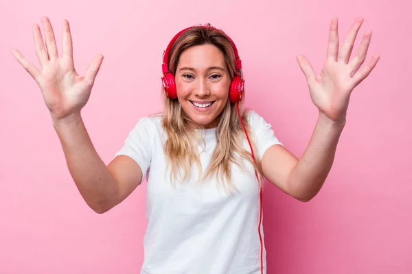若いオーストラリア人女性はピンクの背景に隔離された音楽を聞いて楽しい驚き 興奮し 手を上げる — ストック写真