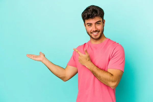 Joven Hombre Caucásico Aislado Sobre Fondo Azul Excitado Sosteniendo Espacio —  Fotos de Stock