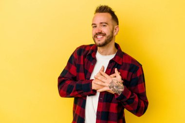 Sarı arka planda izole edilmiş genç, dövmeli beyaz adam dost canlısı bir ifadeye sahip, avuçlarını göğsüne bastırıyor. Aşk konsepti.